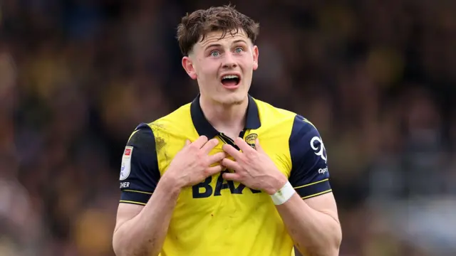 An image of Will Lankshear, wearing his yellow Oxford United home kit, gesturing towards himself during a match against Hull City in April