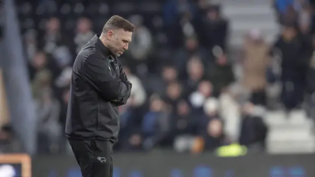 A photo of Derby County boss John Eustace with his arms folded, looking down at the pitch, on the touchline during their game against Wrexham