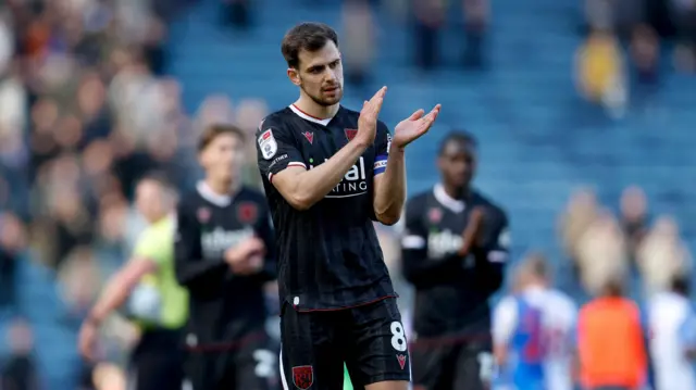 A photo of Jayson Molumby applauding fans in West Bromwich Albion's black and red third kit