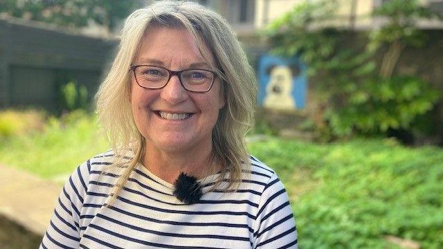 Nicola Masters outside wearing a black and white striped t-shirt and glasses smiling at the camera