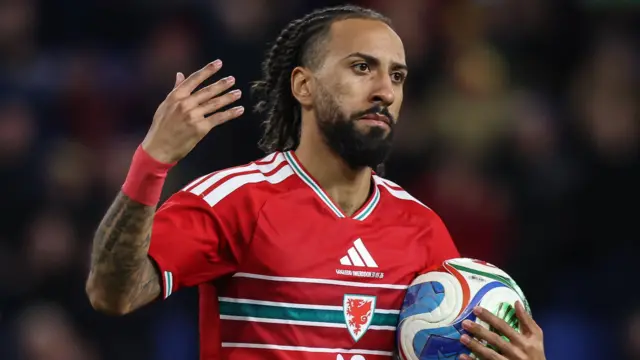 Sorba Thomas, wearing Wales' red home shirt, holds the ball in his left hand and raises his right hand after scoring in the 1-1 draw with Northern Ireland in Cardiff