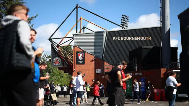 The outside of the AFC Bournemouth stadium. It is a red brick building with black cladding that reads 'AFC Bournemouth' and has a red and black Bournemouth logo on.