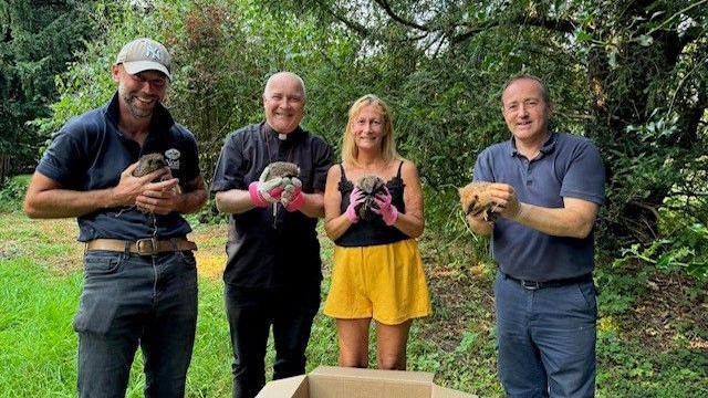 Four hedgehogs are held by four people in the grounds of Bishopthorpe Palace