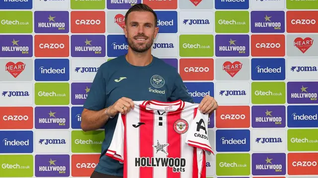Jordan Henderson holding a Brentford home shirt