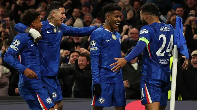 Chelsea players celebrating by a blue corner flag, fans are cheering in the background