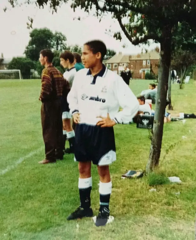 A picture of a boy in full Tottenham kit standing on the touchline