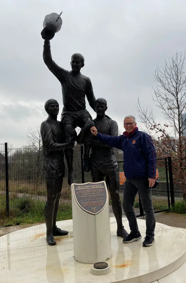 A West Ham fan standing by the statue of Bobby Moore, Geoff Hurst and Martin Peters
