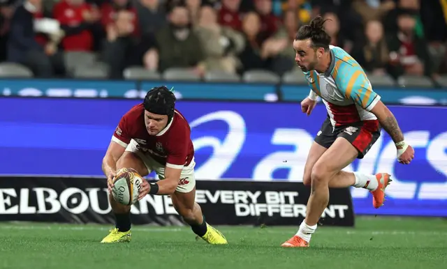 British and Irish Lions' Darcy Graham (L) scores a try under pressure from First Nations & Pasifika XV's Andy Muirhead.