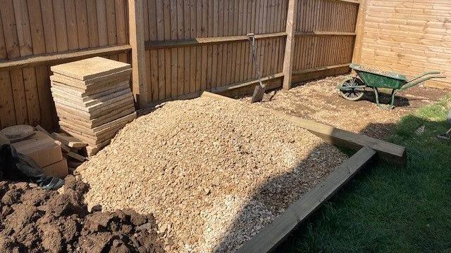 A wheelbarrow and piles of raw material in a garden where work is ongoing