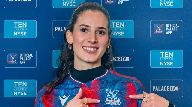 Larisey poses in the Crystal Palace shirt while pointing at the badge