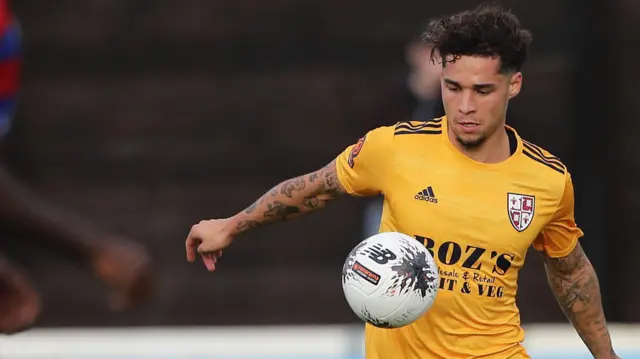 Lewis Walker controls the ball on his chest during a game for Woking. He is wearing a yellow shirt.