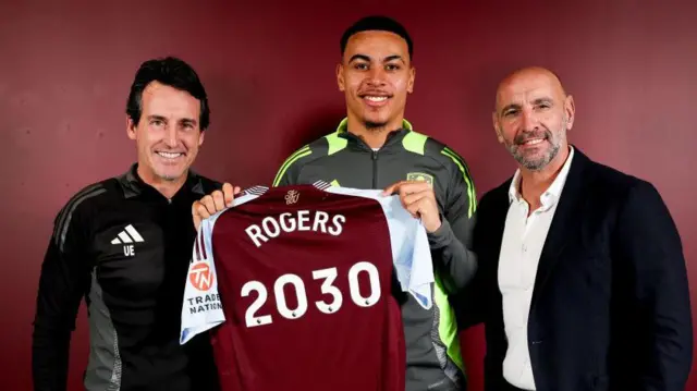 Morgan Rogers with an Aston Villa shirt with "2030" written on it alongside Unai Emery and Monchi