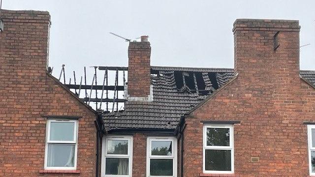 A terraced house with a damaged roof. The roof frame is burnt and exposed after a fire ripped through the top floor of the house.