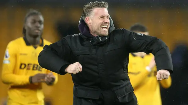 Rob Edwards punching the air in celebration with two Wolves players out of focus in the background