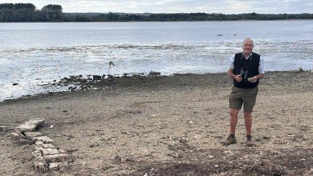 Man stood on the side of Rutland Water, with some old bricks to the left.