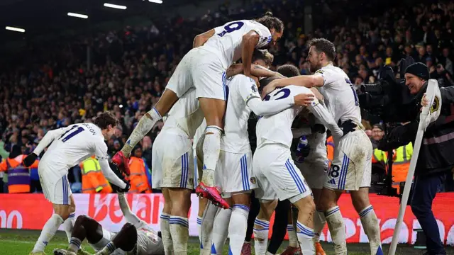 Leeds players celebrating in a huddle next to the corner flag 