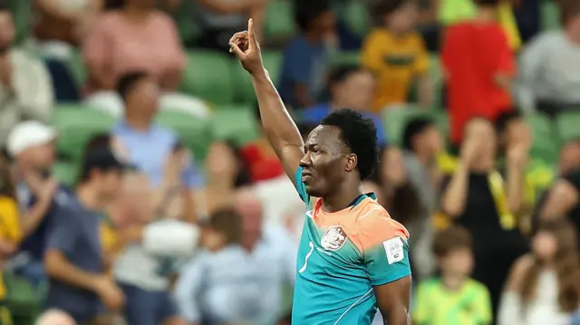 Nestory Irankunda in a green Australia kit with his right arm raised pointing to the sky as he celebrates scoring against Curacao