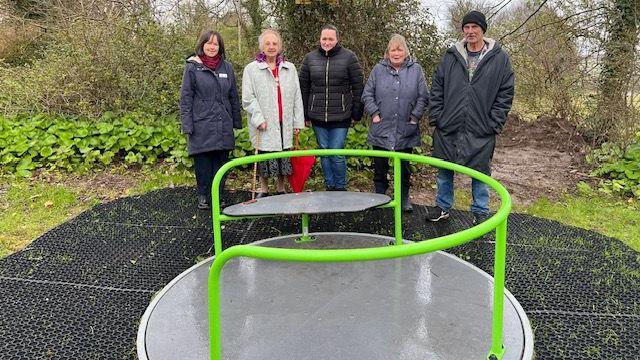 Five adults standing smiling around a roundabout