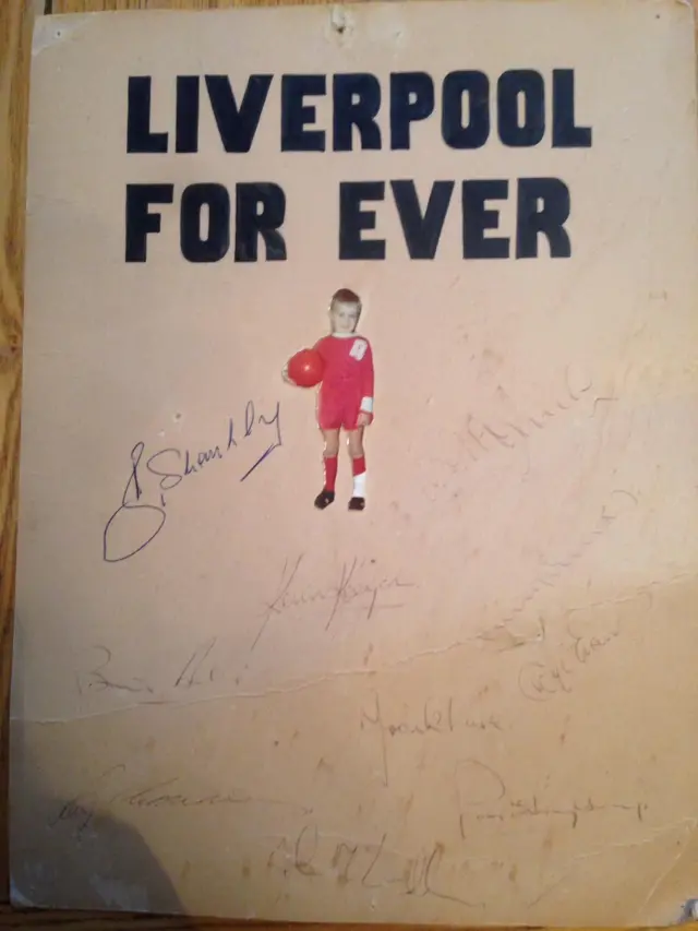 Picture of a young Liverpool fan in Liverpool strip with Liverpool players signitures around it.
