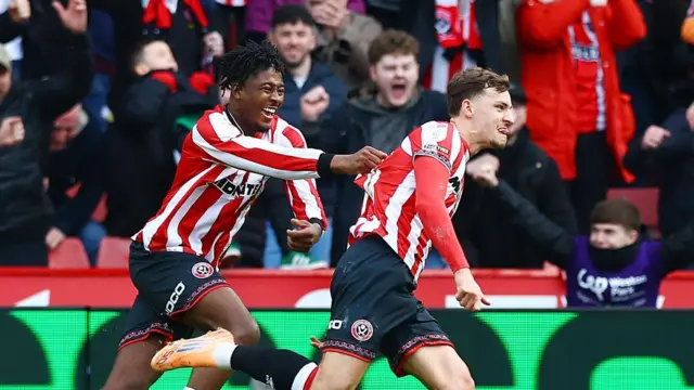 Harrison Burrows races away in celebration after scoring against Sheffield Wednesday as team-mate Andre Brooks grabs hold of the back of his shirt. In the background, fans in the stand at Bramall Lane shout with joy