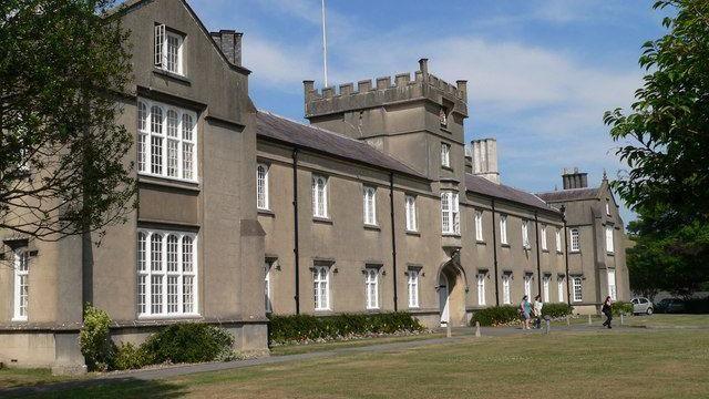 The St David's Building, known as the old building, at the Lampeter Campus. It is grey with a lawn and path in front of it