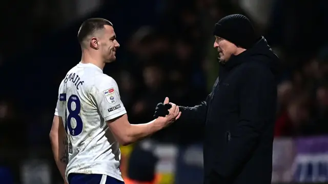 Preston North End striker Milutin Osmajic and boss Paul Heckingbottom, wearing a black hat and jacket, shaking hands after a 3-0 victory against Sheffield Wednesday