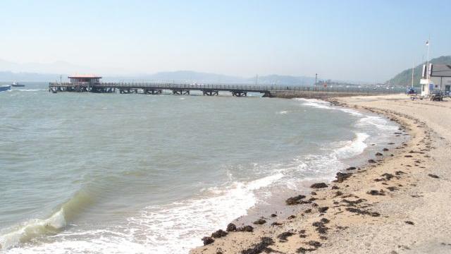 A picturesque pier is shown along the horizon at Beaumaris Beach, North Wales.