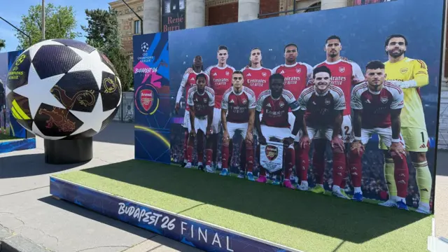 A life-size picture of Arsenal players lining up before a game on a small platform in Budapest