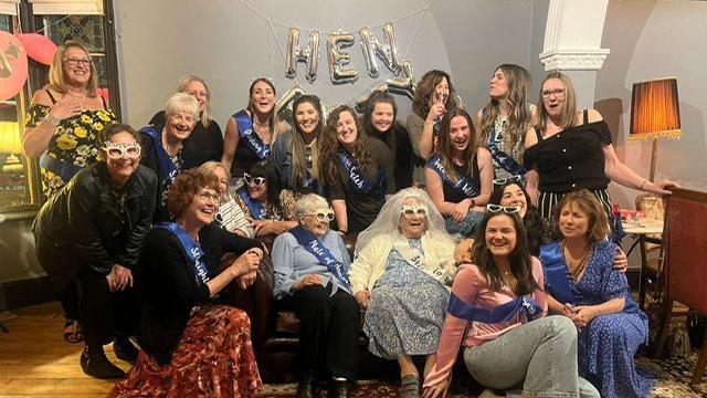 A group of women sit in a bar called Riff Raff in Clevedon and smile at the camera. They are on a hen do and the word "HEN" is spelled out in silver coloured balloons above them