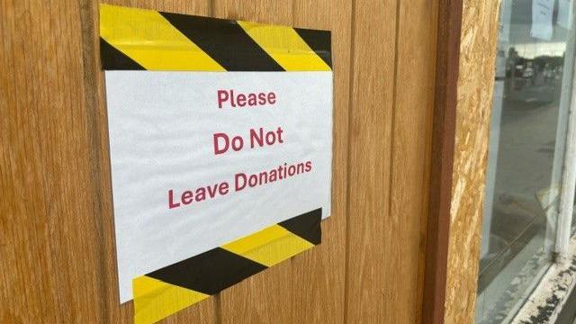 White sign with yellow and black tape that says "Please do not leave donations"