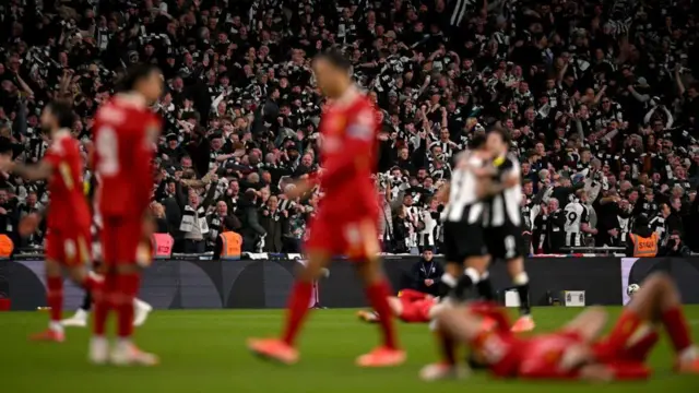 Liverpool players look devastated while Newcastle players and fans celebrate in the background