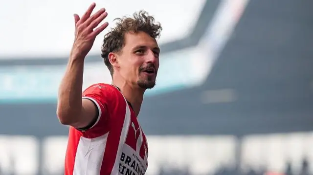 Olivier Boscagli wears a PSV home shirt and lifts one hand to the crowd