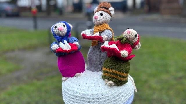 Three more colourful knitted characters from the Charles Dickens' novella, 'A Christmas Carol'. The characters are depicted as mice and sit on a bollard.