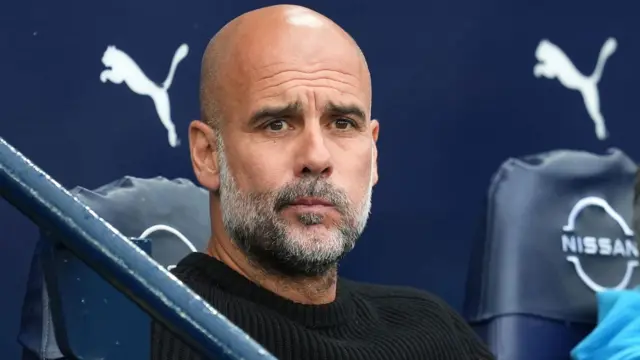 Pep Guardiola sits in the Manchester City dugout