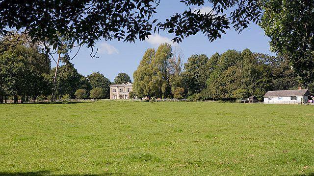 A large meadow with Wintershill Hall in the distance - a large mansion house surrounded by mature trees