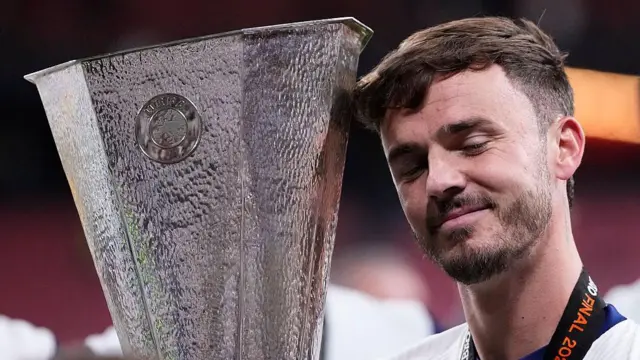 James Maddison holds the Europa League trophy and smirks proudly