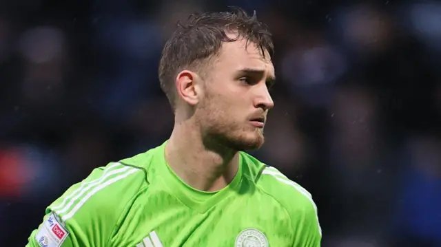 Jakub Stolarczyk, wearing a lime green Leicester goalkeeping top, looks across the camera in front of a blurred black background.