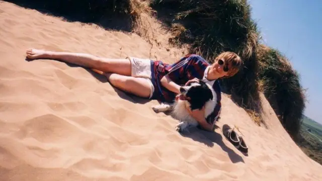 A picture of a teenager on a beach with a black-and-white dog and wearing a Newcastle shirt