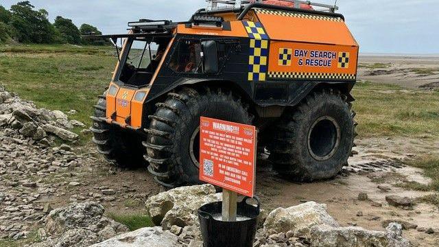 Large all-terrain vehicle on bay with warning sign in front of it.