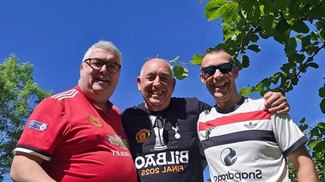 Three men in various Manchester United shirts pose for a picture