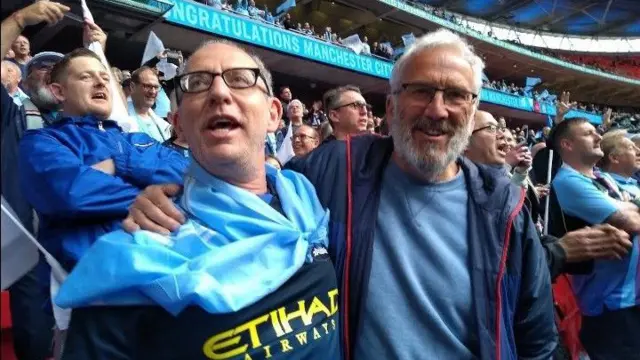 An image of two men cheering on Manchester City at Etihad Stadium