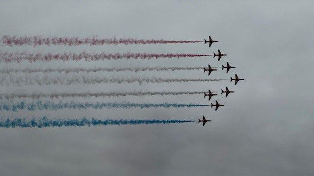 The Red Arrows fly in formation with red white and blue trails following behind them.