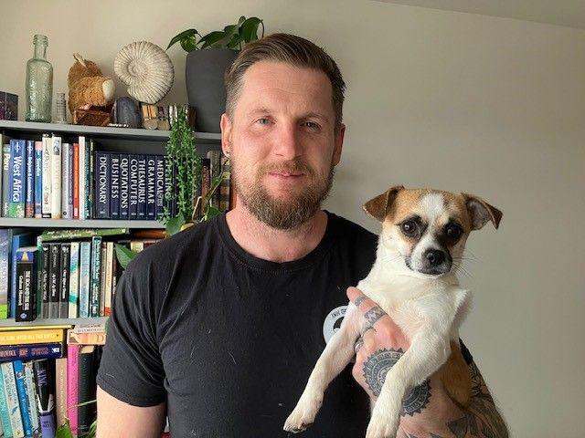 Liam Enisz, who has short brown hair and a beard, is holding Penny up to the camera. 