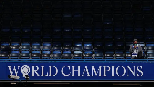 A lone supporter of Chelsea FC sits in the stands above “World Champions” signage inside Stamford Bridge 