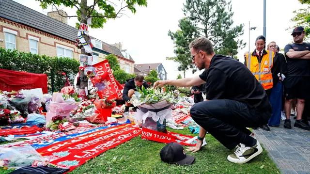 Jordan Henderson crouching down and looking at the tributes left to Diogo Jota