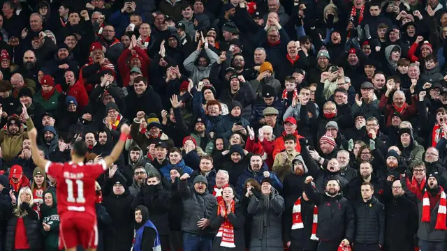 Mohamed Salah, with his back to the camera, saluting Liverpool fans