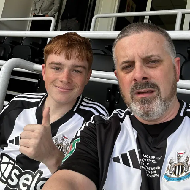 A boy and his father have a selfie in the stands wearing Newcastle kit