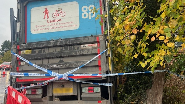 The back of a lorry that has crashed into a wall. Police tape is stretched across the vehicle.