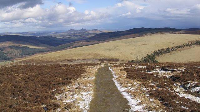 A frost-covered hill track with heather on either side and views of hills stretching into the distance.