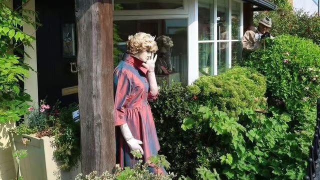 A scarecrow of Princess Diana. It is dressed in a red dress and a blonde wig. One hand is up near the face, disguising from paparazzi
